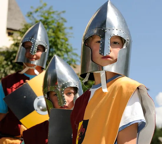 Kinder in mittelalterlichen Ritterkostümen mit Helmen und Schilden bei einer historischen Nachstellung